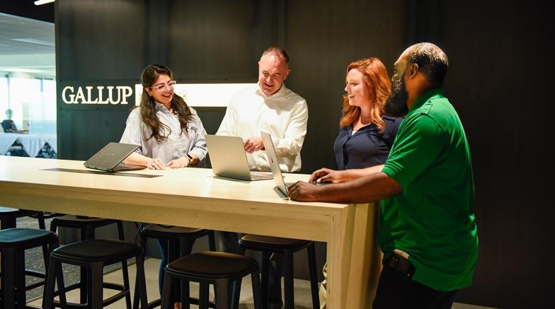 Four people at a standing desk with a laptop having a group meeting.