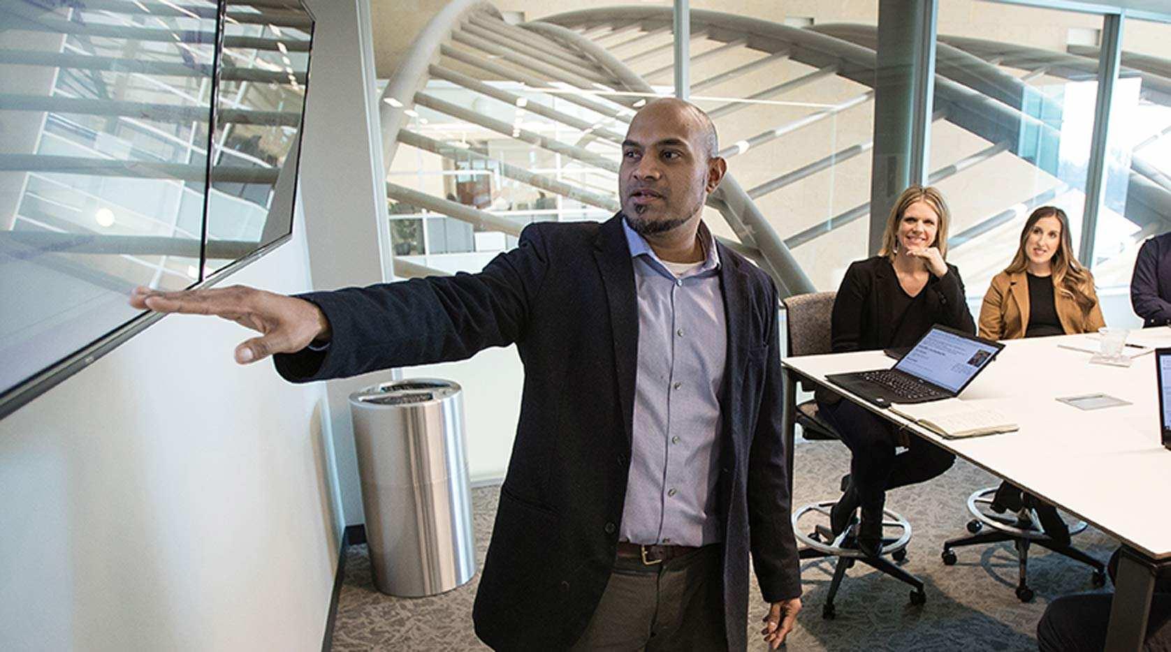 Employee presenting on a video display in the front of a conference room.