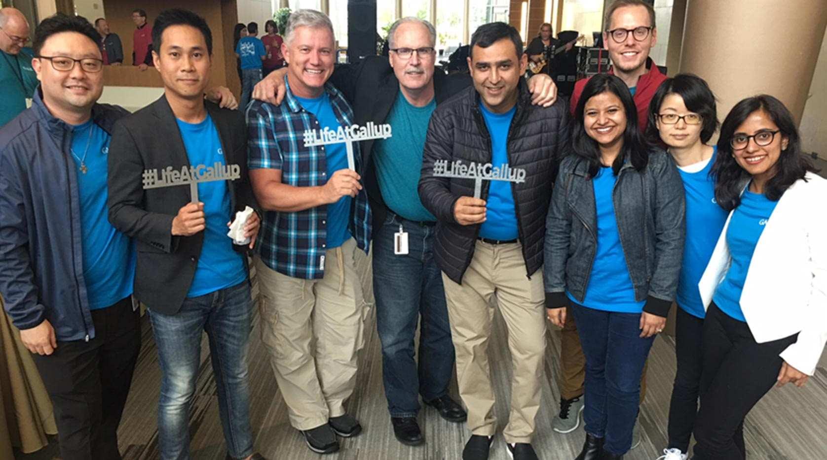 A group of Gallup employees grouped together some holding up #LifeAtGallup signs.