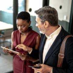 A male and female coworker looking at a tablet and discussing work expectations.