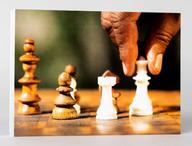 Front of a card, showing a hand moving a chess piece on a chess board.